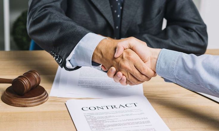 Two professionals shaking hands over a contract document on a desk, symbolizing a finalized agreement — highlighting how one contract mistake can impact a startup’s funding and legal future.